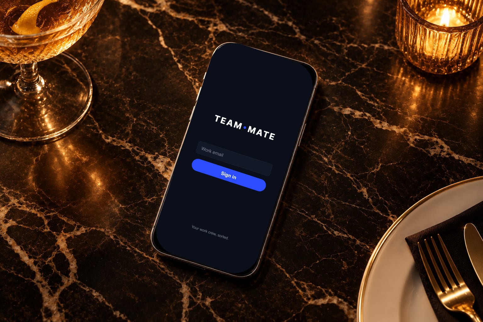 A phone showing the TEAM MATE sign-in screen on a restaurant table at night